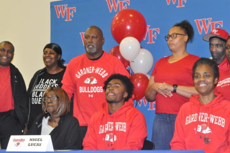Senior Nigel Lucas (seated) signs at his signing ceremony with father coach Reginald Lucas standing behind him. 